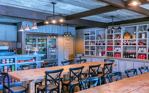A dining area with tables, chairs, shelves, and a fridge.
