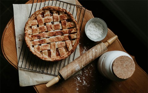 A lattice-topped pie on a cooling rack with a rolling pin and flour.