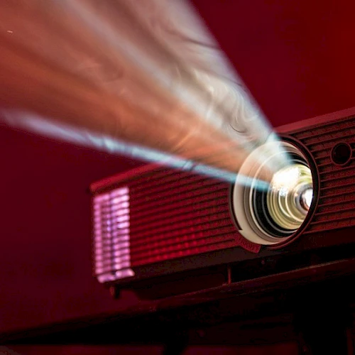 A projector emits a bright beam of light in a dark room, casting a vibrant glow across its surroundings.