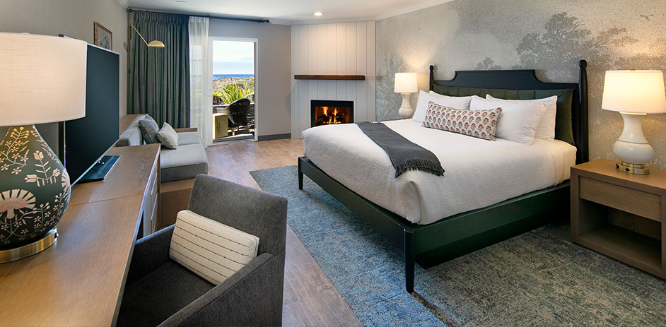A hotel room with a bed, fireplace, balcony, TV, and seating area.