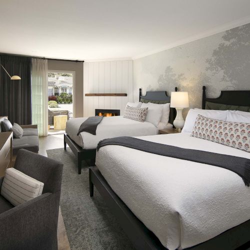 A modern hotel room with two queen beds, a desk and chair, a seating area, a TV, lamps, and a balcony door opening to outside.