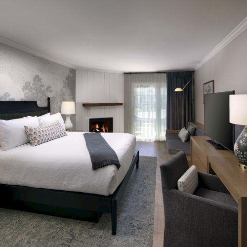 A modern hotel room with a king bed, two nightstands, a sofa, a desk, a fireplace, and soft lighting in neutral tones. Ends here.