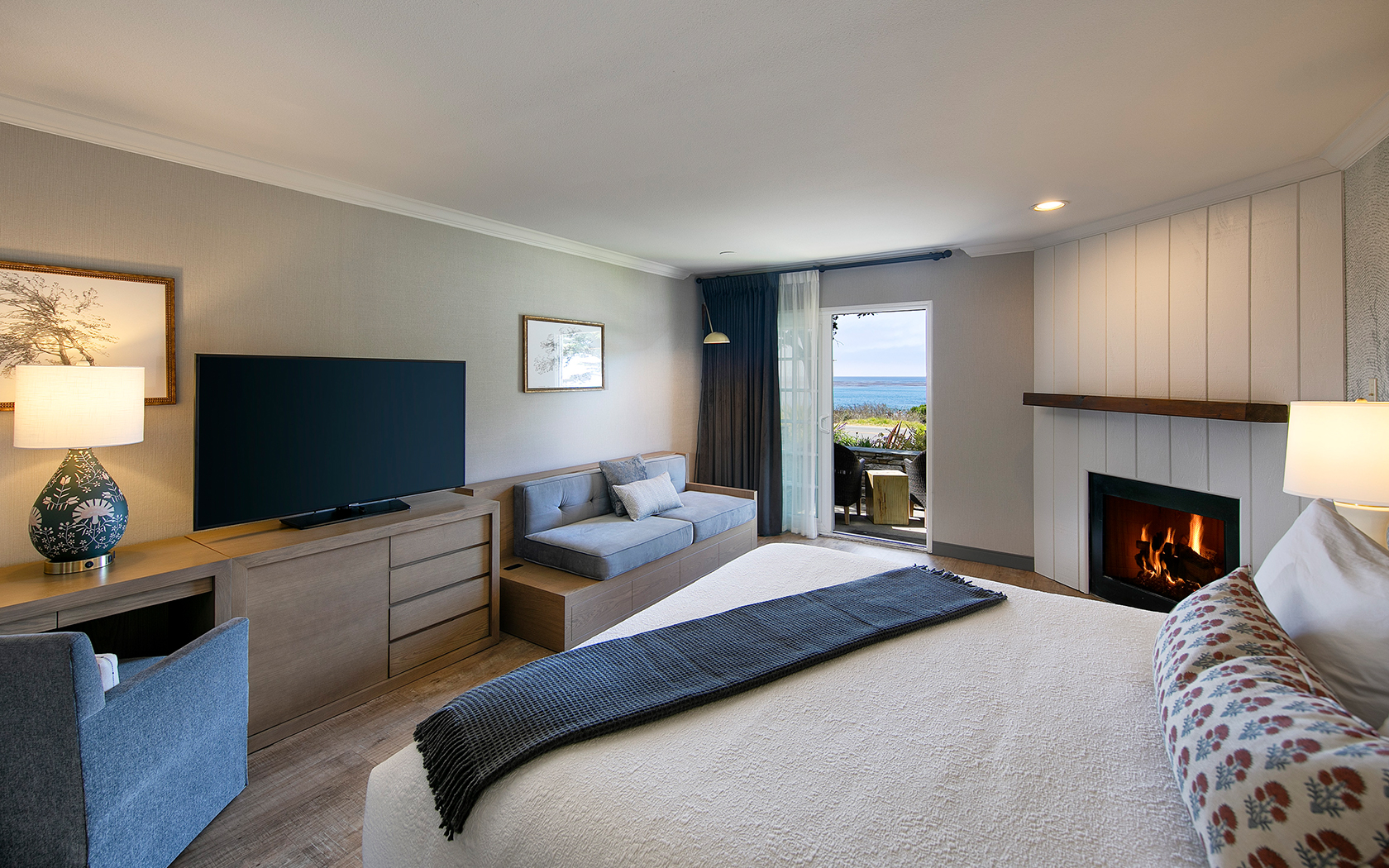 A wide view of a hotel room with a bed, fireplace, TV, and sofa.