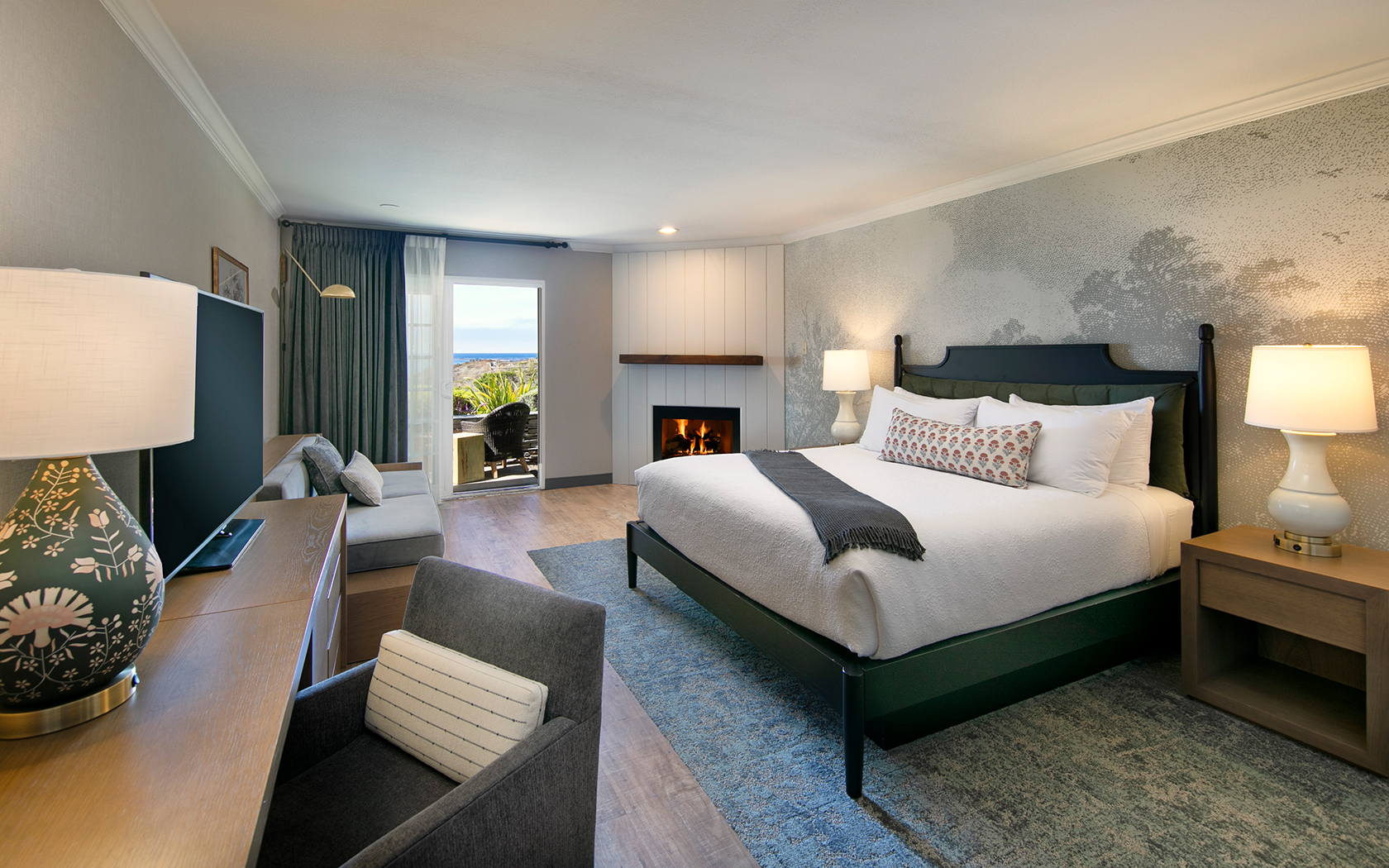 A wide view of a hotel room with a bed, fireplace, and window.