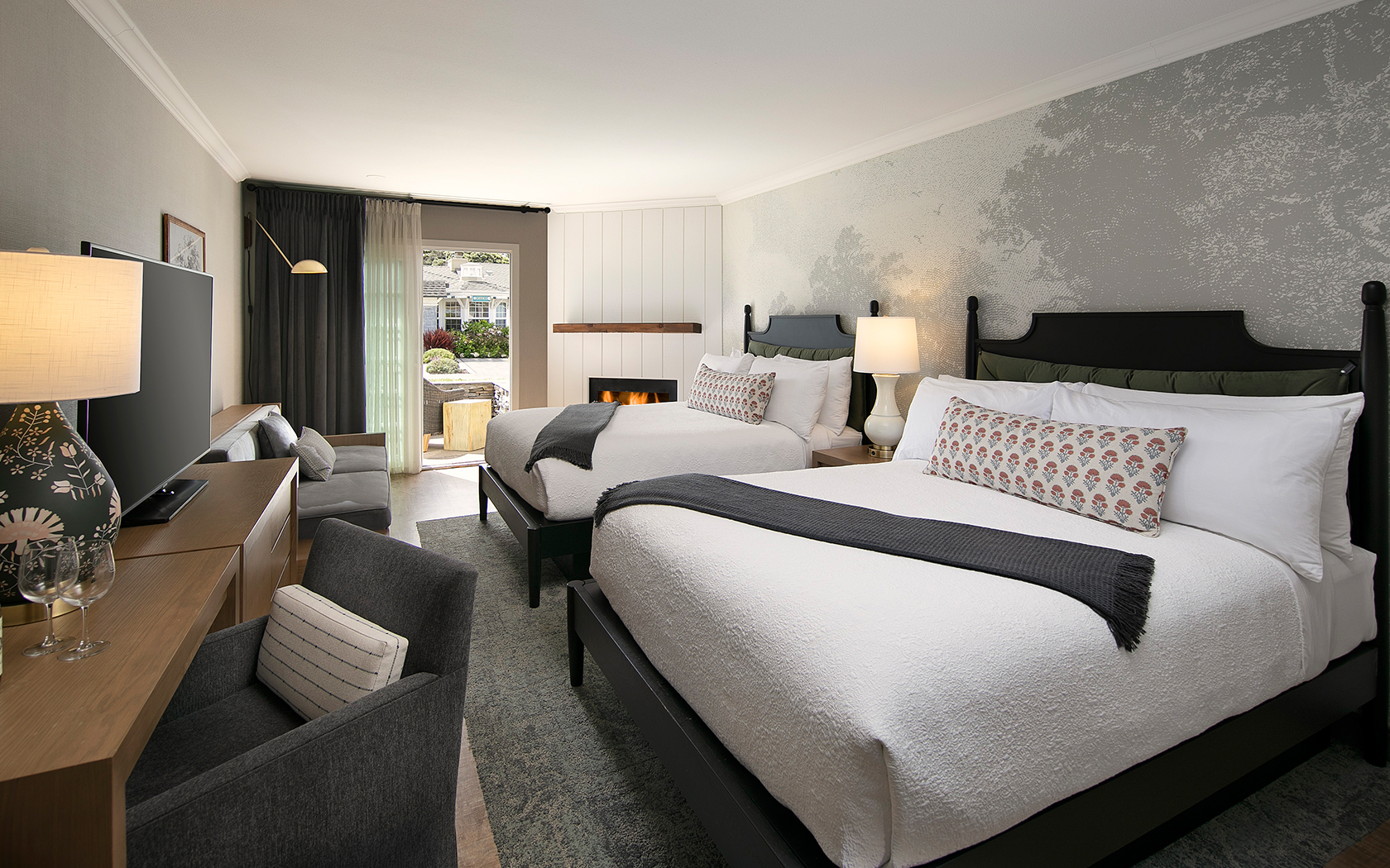 A hotel room with two beds, a fireplace, a window, a TV, and a seating area.