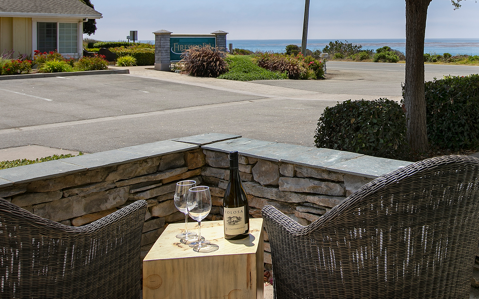 a patio with two wicker chairs and a wooden table with a bottle of wine and two glasses