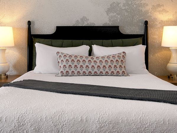 A neatly made bed with white linens, a textured throw, decorative pillows, and two matching bedside lamps glowing softly.