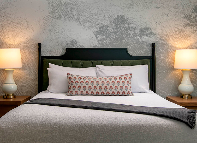 A neatly made bed with a green headboard, white pillows, and a patterned pillow in the center.
