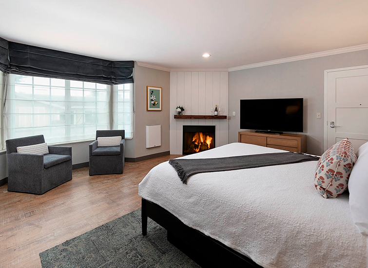 A wide view of a hotel room with a large bed, fireplace, seating area, and TV.