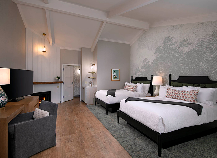 A hotel room with two beds, a TV, fireplace, and doorway.