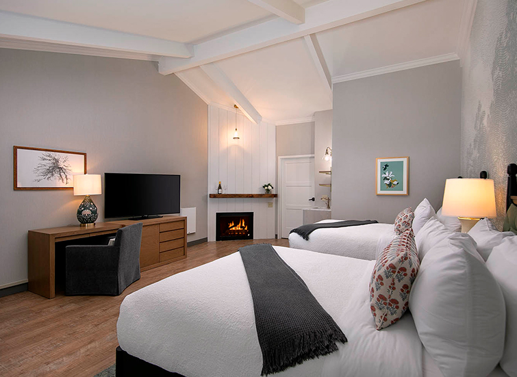 A wide view of a hotel room with two beds, a fireplace, and a desk with a TV on it.