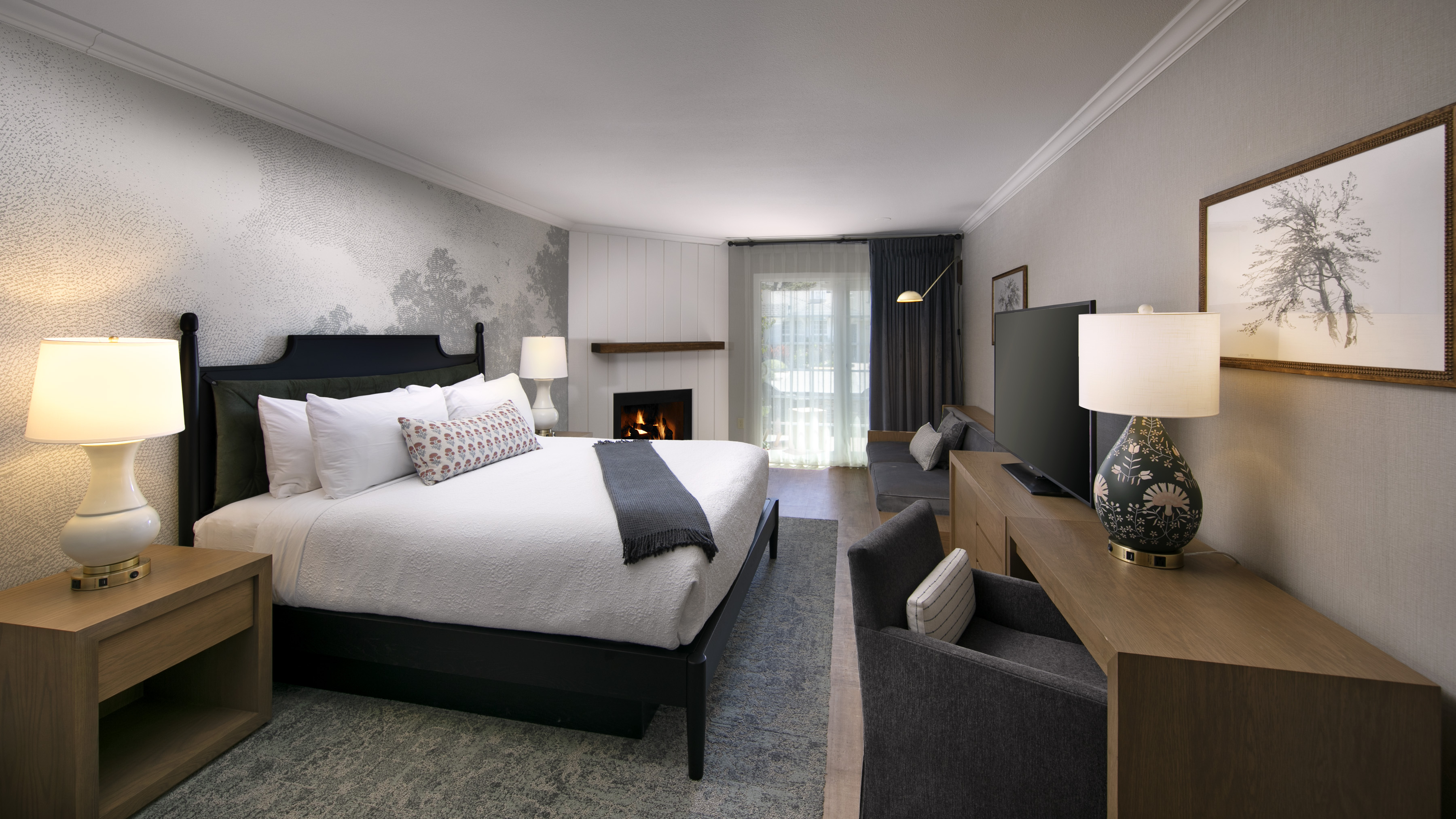 A wide view of a hotel room with a king-size bed, fireplace, seating area, and flat-screen TV.