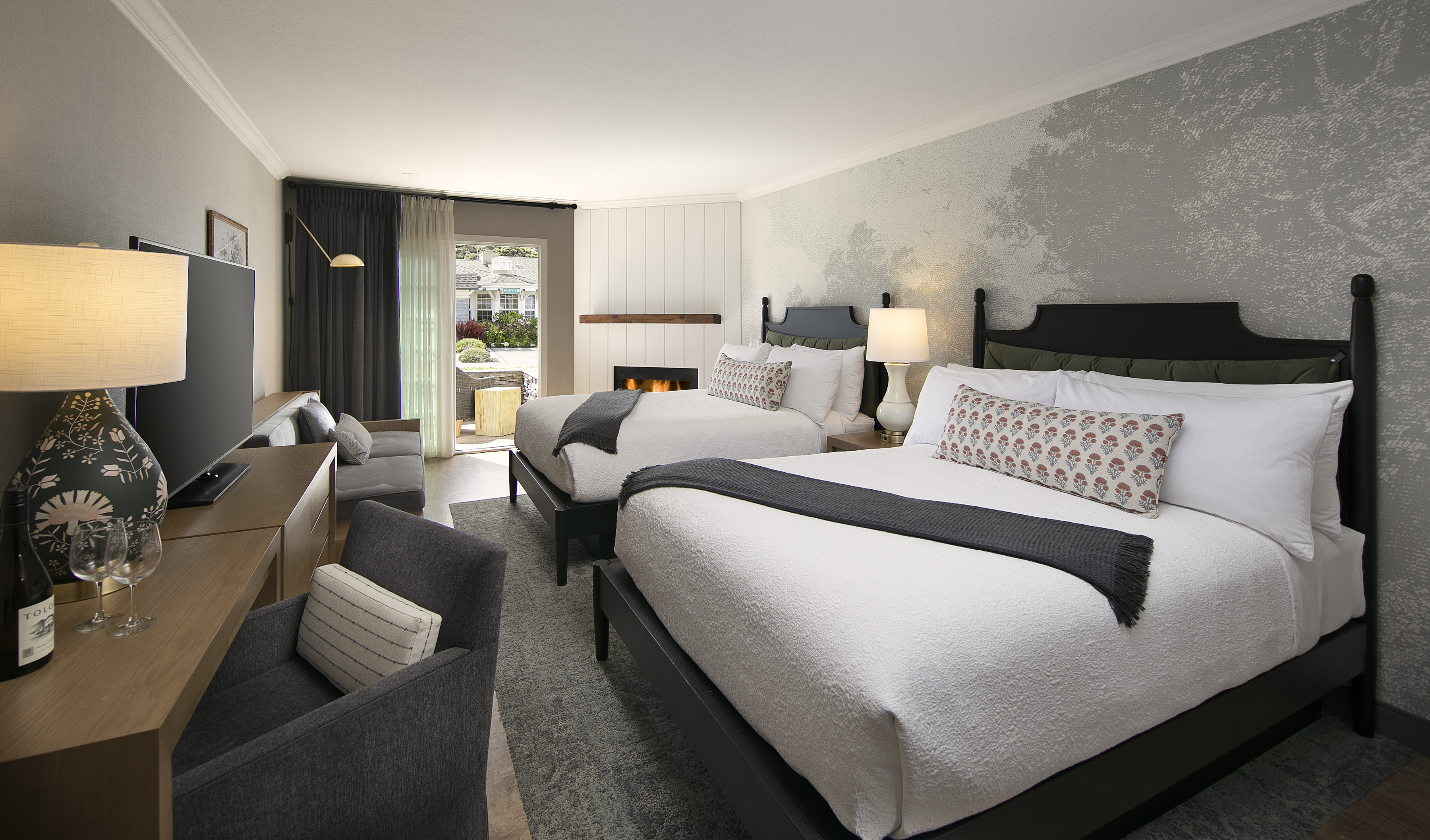 A hotel room with two beds, a fireplace, a TV, and a chair.